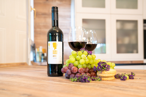 Rotwein der Marke Schmeckerei mit Trauben, Lavendel und Gebäck auf Holztisch.