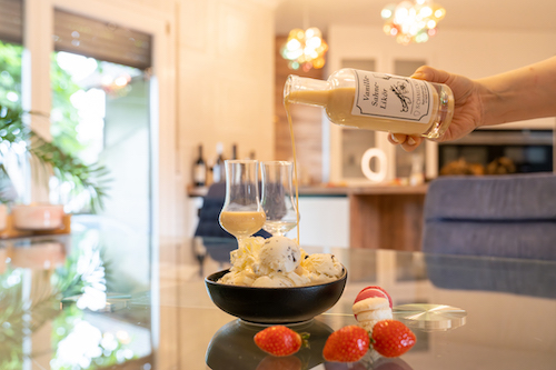 Cremiger Likör wird über Vanilleeis gegossen, umgeben von Erdbeeren und Macarons.