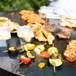 Gemischte Grillplatte mit Fleisch, Lachs, Gemüsespießen und Saucen auf einer Plancha.