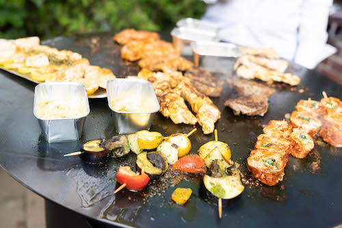 Gemischte Grillplatte mit Fleisch, Lachs, Gemüsespießen und Saucen auf einer Plancha.